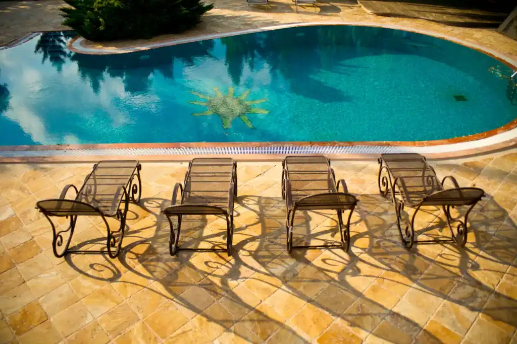 Bright backyard swimming pool with a decorative tile motif, surrounded by elegant lounge chairs and stone paving, perfect for outdoor relaxation and pool parties.