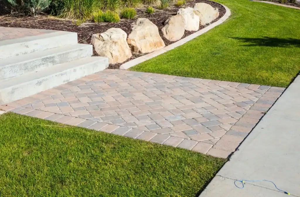 Stamped concrete patio with stone accents, well-manicured grass, and landscaped rock border, ideal for outdoor entertaining and enhancing backyard aesthetics.