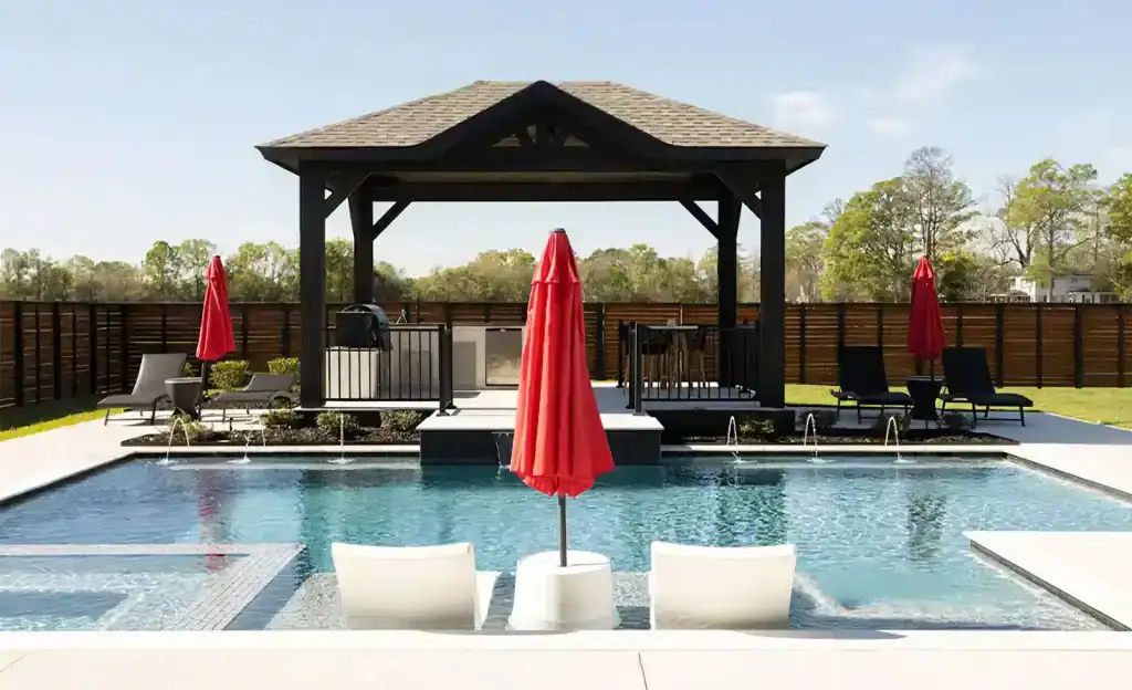 Spacious backyard pool area with a modern outdoor gazebo, surrounded by lounge chairs and vibrant red umbrellas, perfect for relaxing and entertaining.