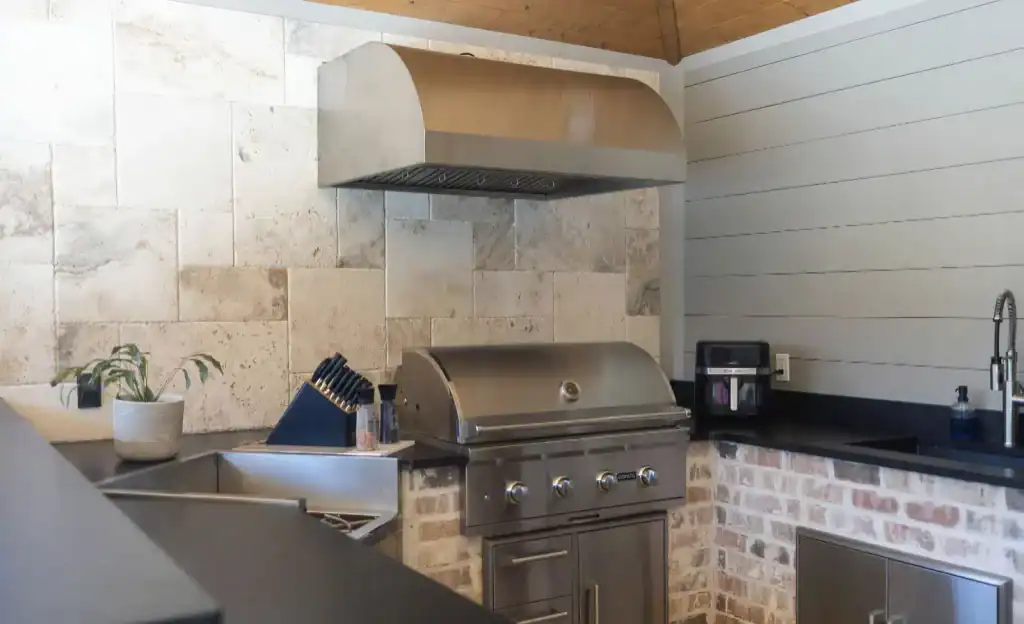 Modern outdoor kitchen with stainless steel grill, stone and brick accents, and black countertop, perfect for entertaining and outdoor cooking.