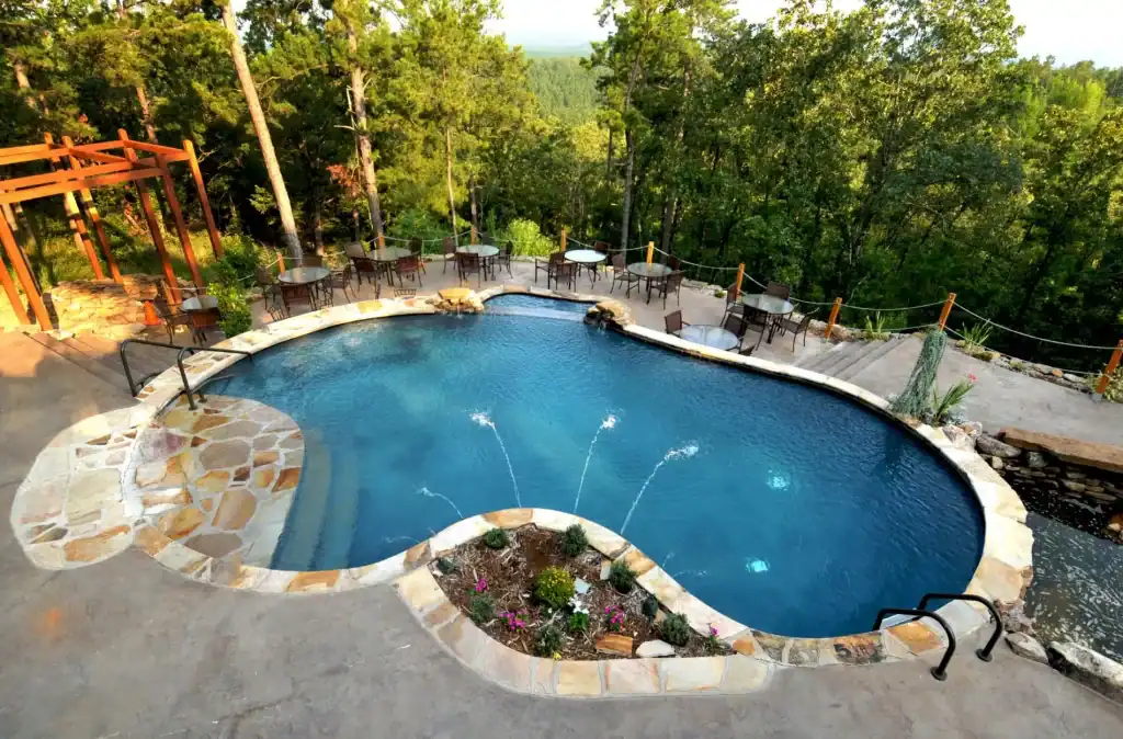 Luxurious backyard pool with natural stone edging, surrounded by lush trees and outdoor seating, perfect for relaxing and entertaining amidst scenic forest views.