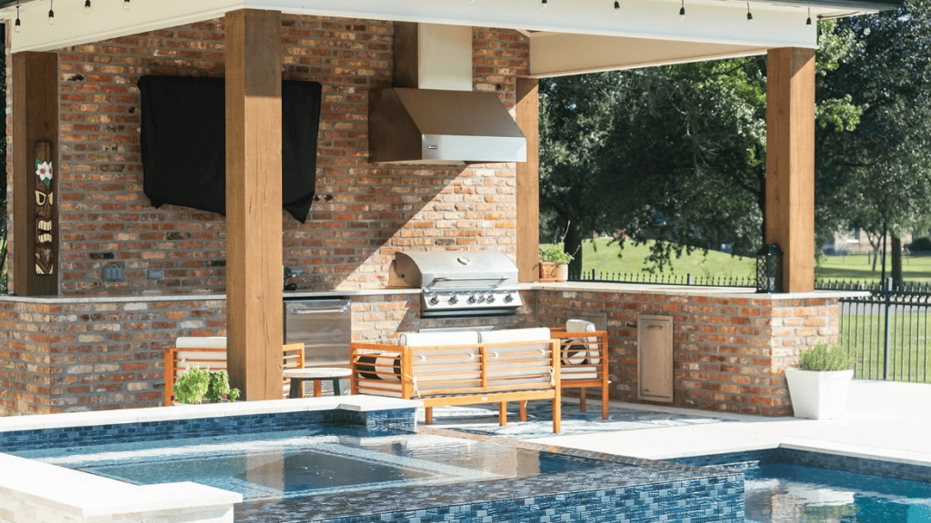 Beautiful outdoor kitchen with built-in grill, brick accents, and a swimming pool, perfect for outdoor entertaining and relaxation.