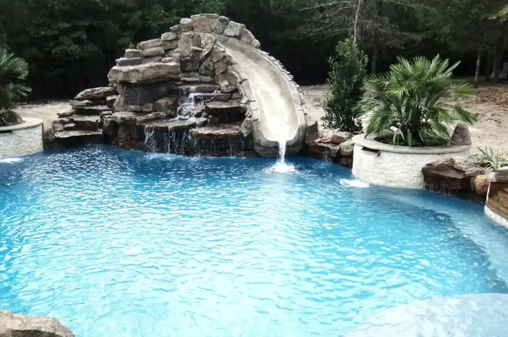 Luxurious in-ground backyard pool with rock waterfall feature, surrounded by lush greenery for a perfect outdoor relaxation spot.