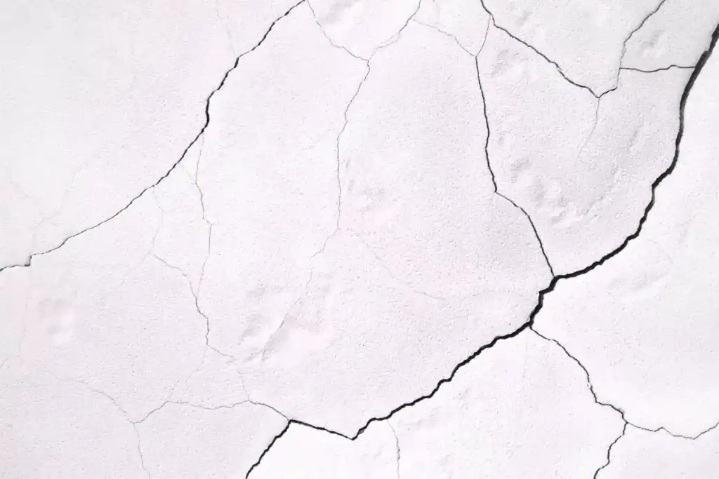 Cracked white wall with visible black and gray fissures, close-up image.