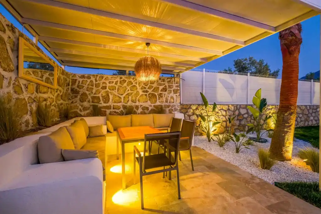 Luxurious backyard patio with cozy seating area, ambient lighting, stone wall accent, and lush plants, perfect for relaxing and entertaining near your custom-built pool.