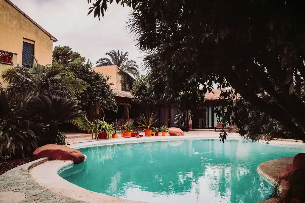 A luxurious backyard swimming pool surrounded by lush tropical plants and trees, featuring a curved shape, stone accents, and a relaxing outdoor atmosphere perfect for leisure and entertaining.