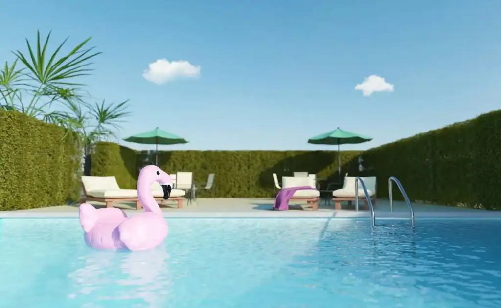 Pink inflatable flamingo float in a backyard swimming pool with clear blue water and modern lounge chairs under green umbrellas, perfect for relaxing and enjoying a sunny day.