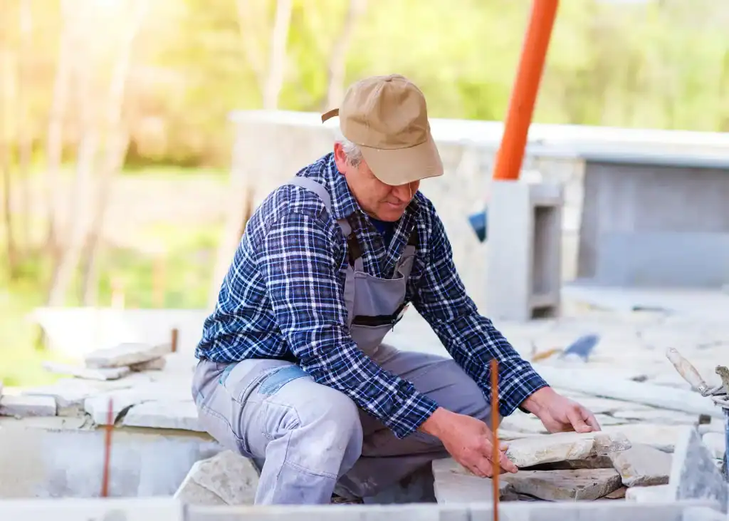 High-quality pool builder working on stonework at an outdoor construction site to create custom swimming pools for clients.