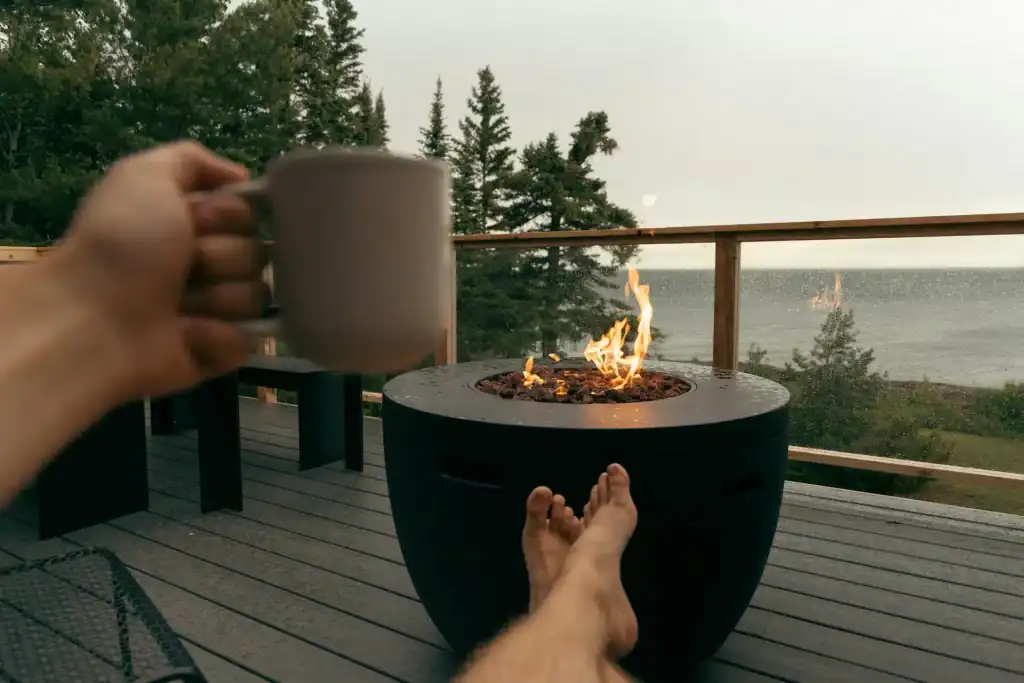 A person enjoying a relaxing moment on a wooden deck by a modern fire pit with ocean views in the background. The scene captures serenity and the perfect outdoor setting for leisure and entertainment.