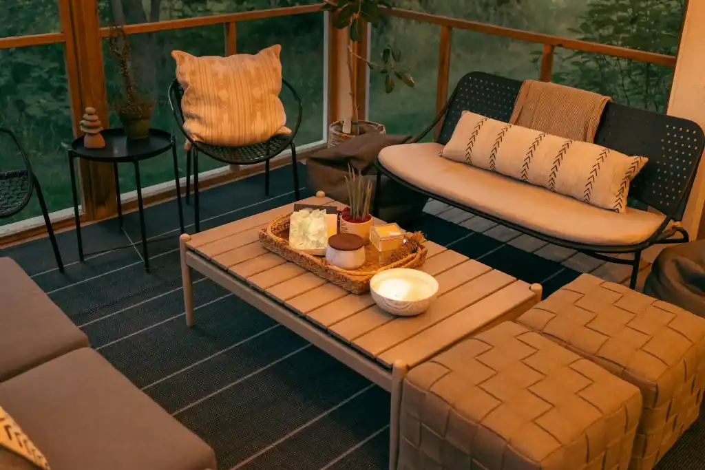 Cozy outdoor porch seating area with comfortable sofas, chairs, and a coffee table surrounded by greenery, perfect for relaxing and entertaining.