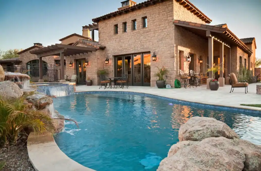 Luxurious backyard with a stunning freeform swimming pool featuring a waterfall and rock accents, perfect for relaxation and entertaining in a beautiful stone house setting.