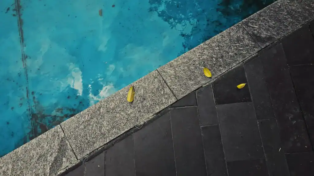 A close-up of a swimming pool edge with yellow fallen leaves on the stone border, showcasing a sleek design and tranquil water surface, perfect for backyard relaxation and luxury pool creations.