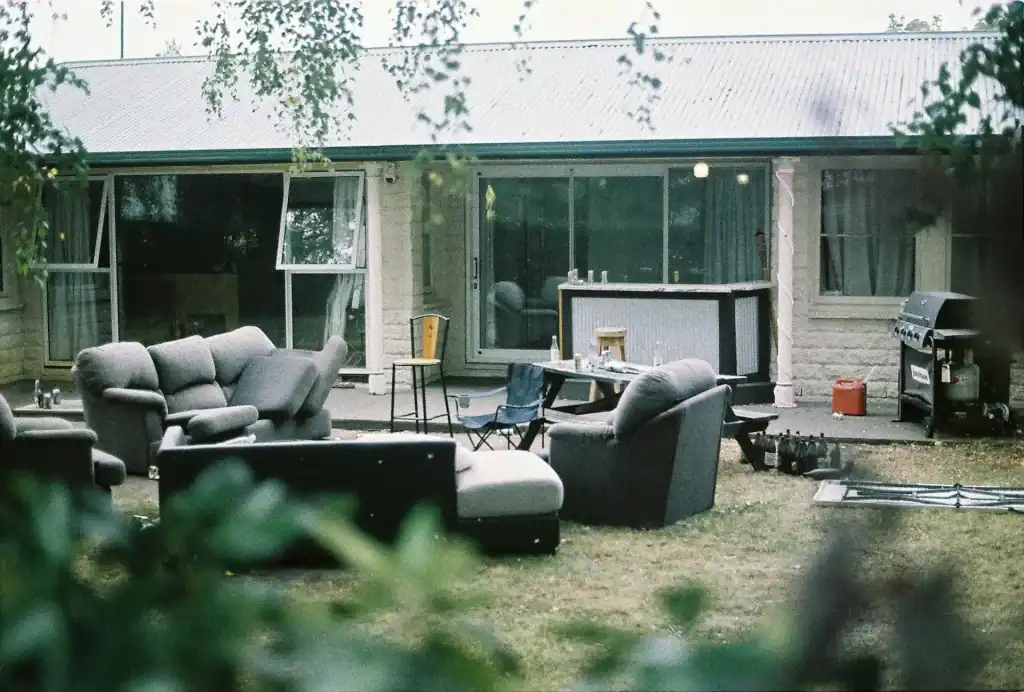 A cozy backyard patio with outdoor seating, a bar area, and a barbecue grill in front of a single-story house, showcasing a relaxing space perfect for entertaining and enjoying outdoor leisure.