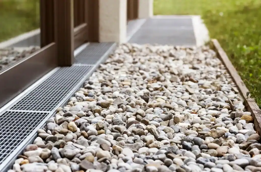 - Pebble stone walkway with drainage system near a building entrance, enhancing outdoor aesthetic and functionality.
