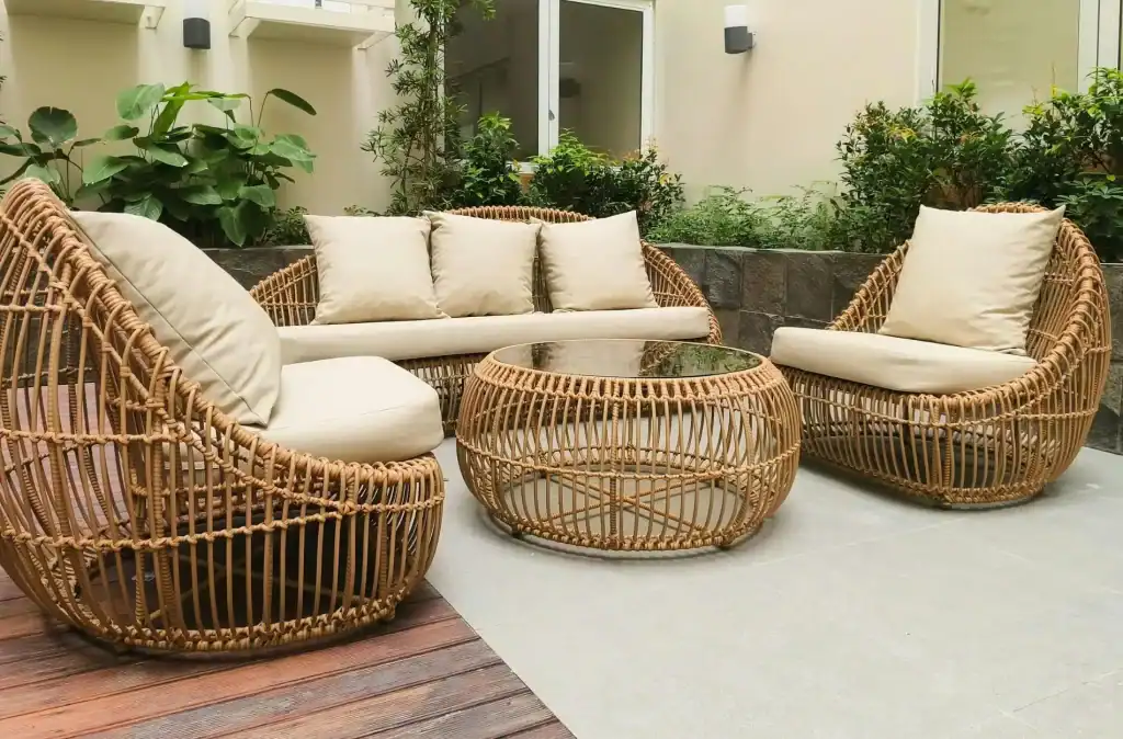 Modern outdoor patio with stylish rattan furniture, including a sofa, armchairs, and a coffee table with a glass top, set in a lush garden area for relaxing and entertaining.