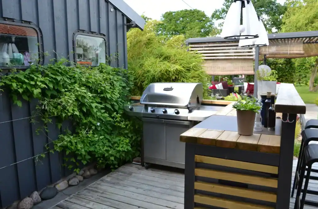 Luxurious outdoor kitchen with stainless steel grill, wooden counter, and green foliage for a perfect poolside entertaining area.