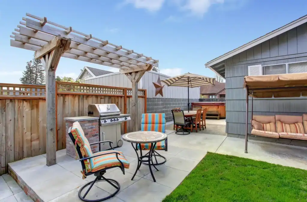 Beautiful backyard patio with outdoor furniture, BBQ grill, shaded swing, and hot tub under a pergola, perfect for relaxing and entertaining in a suburban home.
