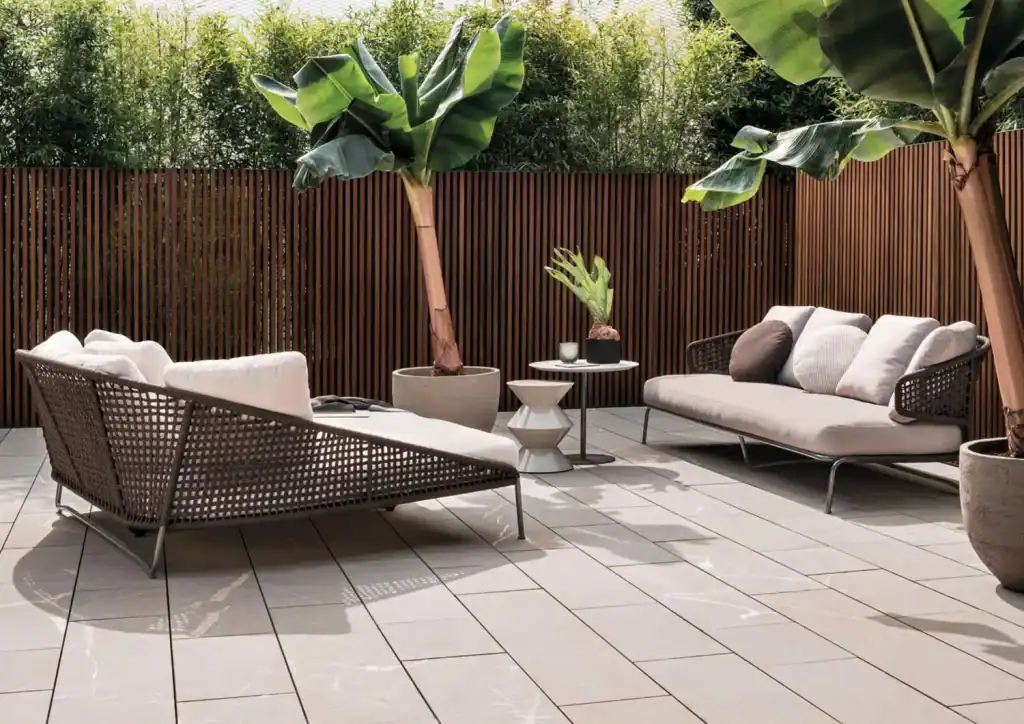Lush tropical plants and stylish outdoor seating create a serene, inviting backyard space for relaxation. The elevated wooden privacy fence adds a modern touch to this tranquil outdoor area.