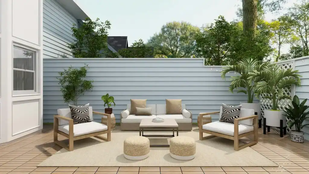 Cozy outdoor patio with modern white seating, lush potted plants, and a neutral-toned rug against a light blue horizontal siding wall, perfect for relaxing and entertaining.
