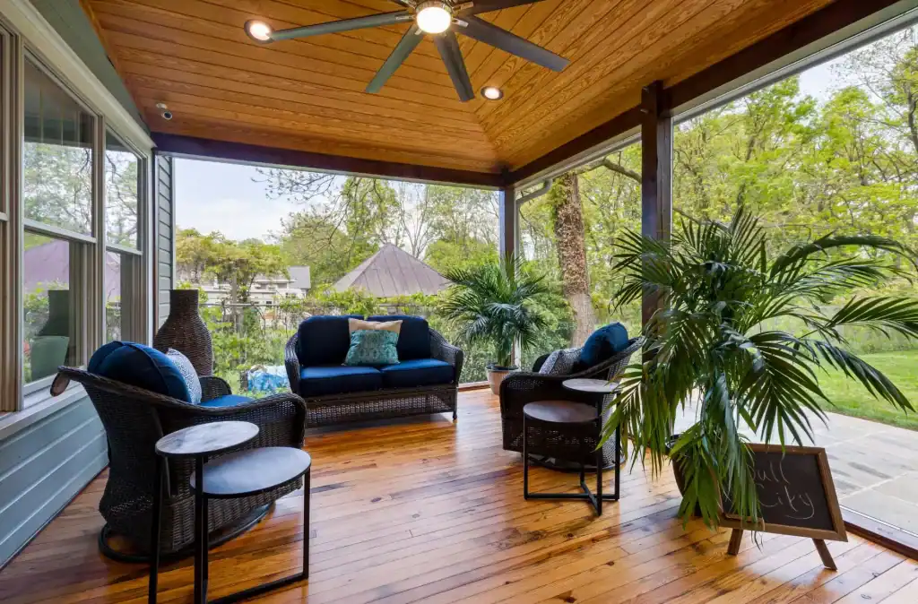 Luxurious screened-in porch with wooden ceiling, ceiling fan, wicker furniture, and lush greenery, perfect for relaxing and enjoying outdoor views.