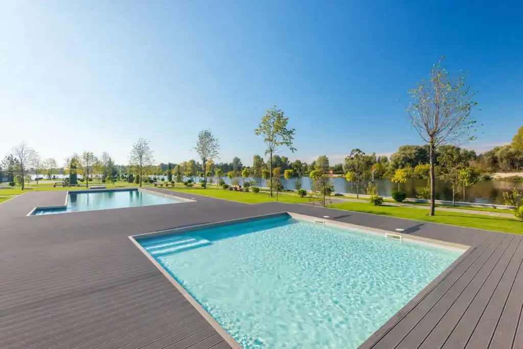 Luxury outdoor swimming pools with modern decking, overlooking a serene lake and surrounded by lush trees, perfect for relaxation and backyard entertainment.