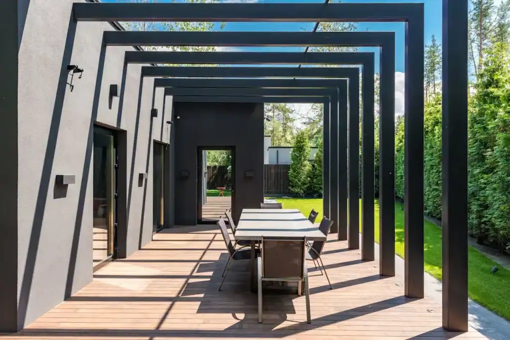 Modern outdoor patio with black pergola, wooden deck, and contemporary furniture, perfect for outdoor gatherings and relaxation in a private backyard.