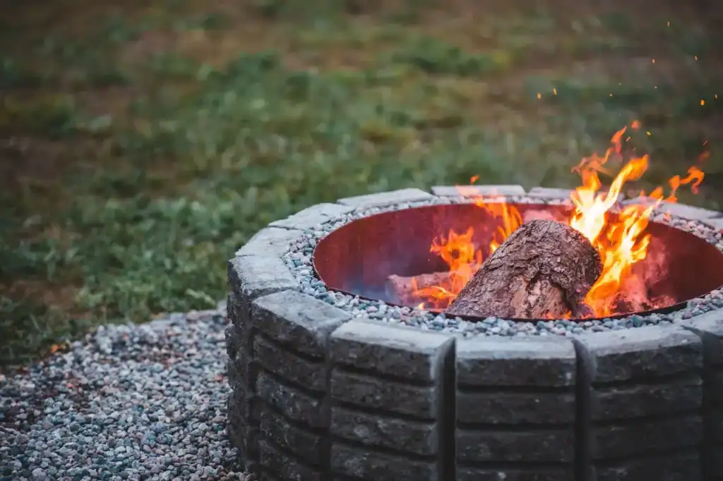 Warm outdoor fire pit with a burning log, surrounded by small pebbles and lush green grass, perfect for relaxing backyard gatherings and enhancing outdoor living spaces.