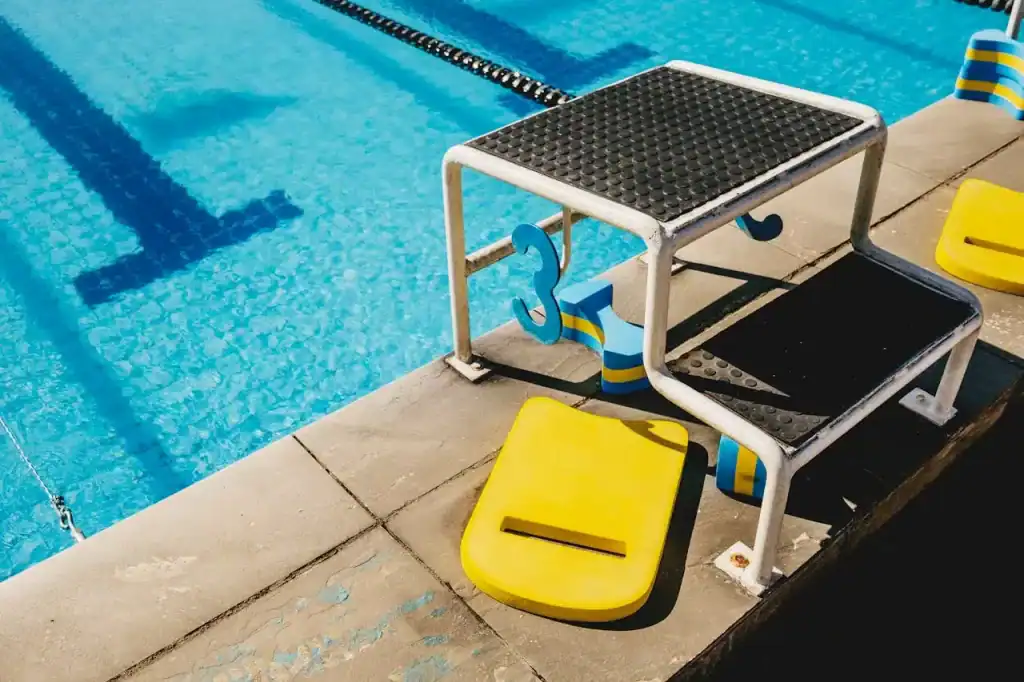 Pool starting block with yellow and black supports next to a sparkling blue swimming pool, ready for competitive swimming races.