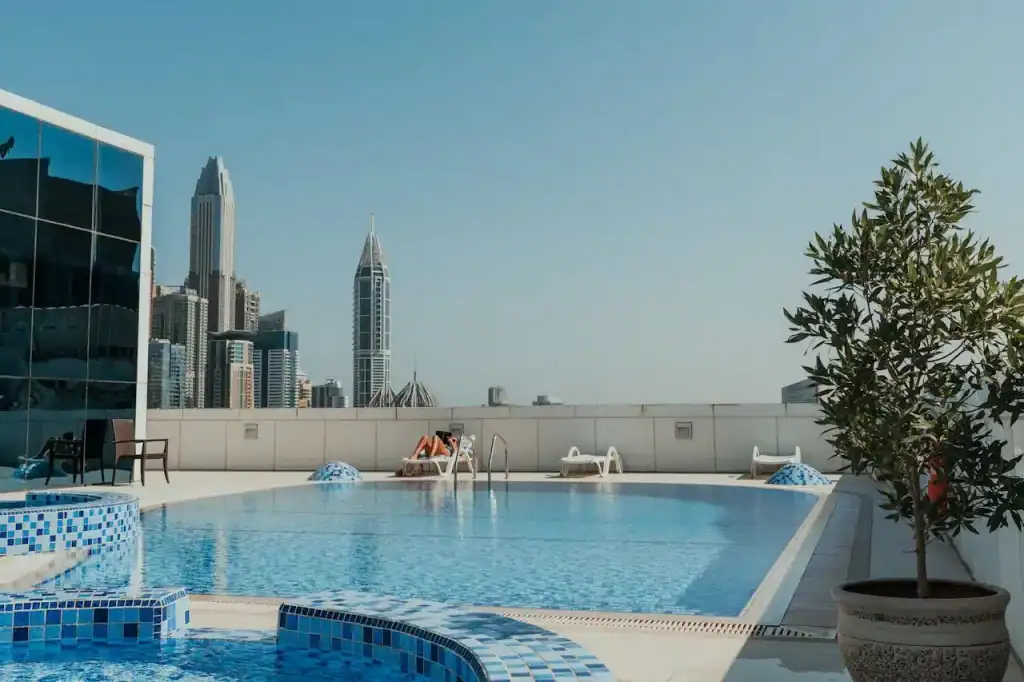 Luxury rooftop swimming pool with city skyline view, featuring blue mosaic tiles, lounge chairs, and a potted tree, perfect for relaxing and enjoying urban living.