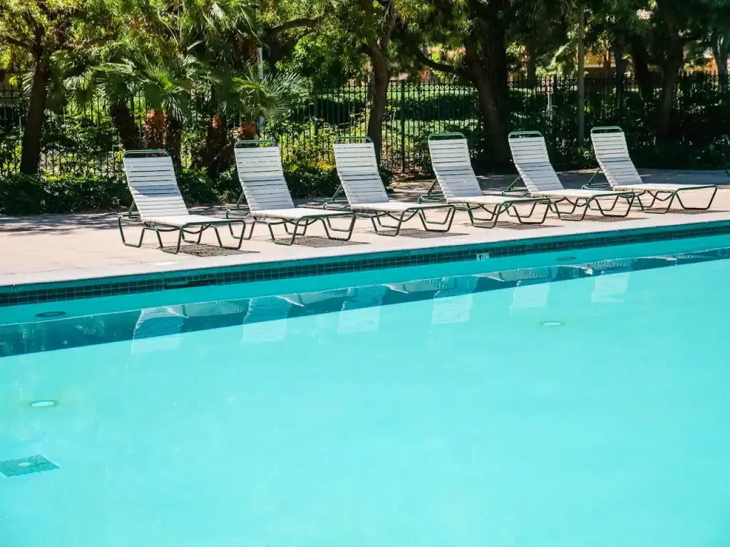 Beautiful outdoor swimming pool with white lounge chairs, lush green trees, and a peaceful ambiance for relaxing and enjoying sunny days.