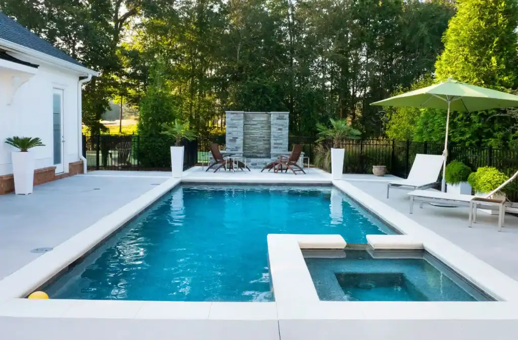 Luxurious backyard pool with hot tub, modern landscaping, white patio, and shaded lounge area, perfect for relaxing and entertaining.