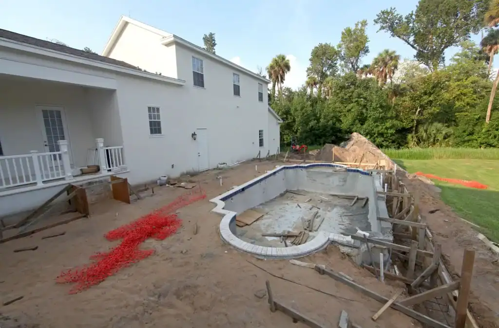In-ground pool construction site with a partially built pool, surrounded by a backyard with a white house and lush greenery, ready for a custom pool installation.