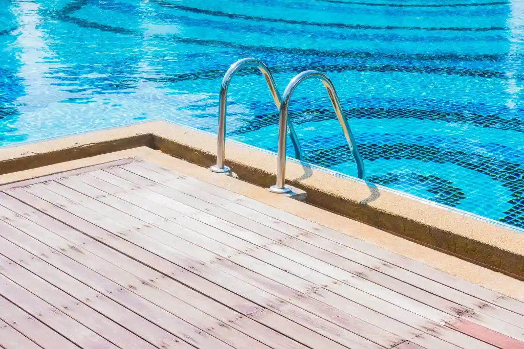 Modern backyard swimming pool with stainless steel ladder, surrounded by a wooden deck for relaxing outdoor leisure.