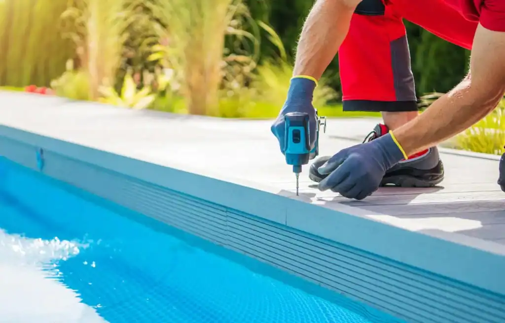 Drip installation of pool decking by a professional worker using a cordless drill outdoors, showcasing quality craftsmanship for custom-designed swimming pool surroundings.