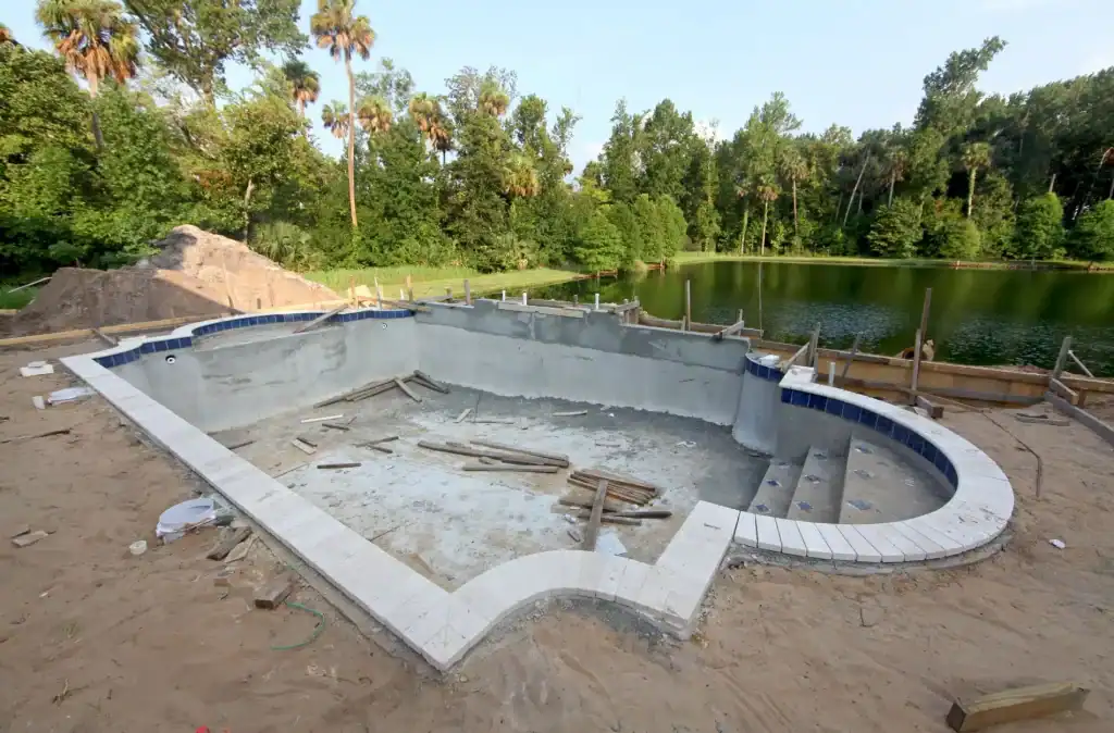 Excavation of a residential in-ground pool under construction by Duplessis Builders, with surrounding wooden framing and a scenic lake view, ready for finishing.