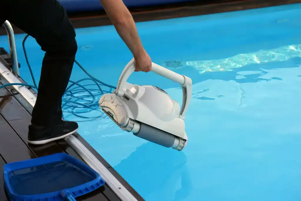 Deep clean of a residential swimming pool using a robotic pool cleaner, with cleaning supplies nearby and clear blue water.