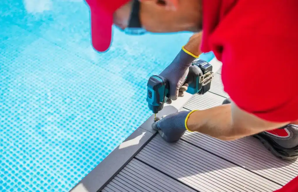 Seaside pool construction worker installing pool edge with power drill, focusing on decking and edging to create a custom pool design.
