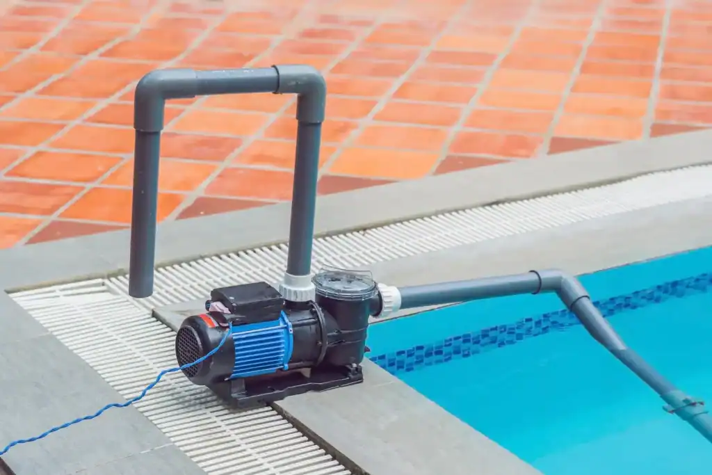 Automatic pool cover pump system installed at edge of clear blue swimming pool, with tiled deck and drainage grate.