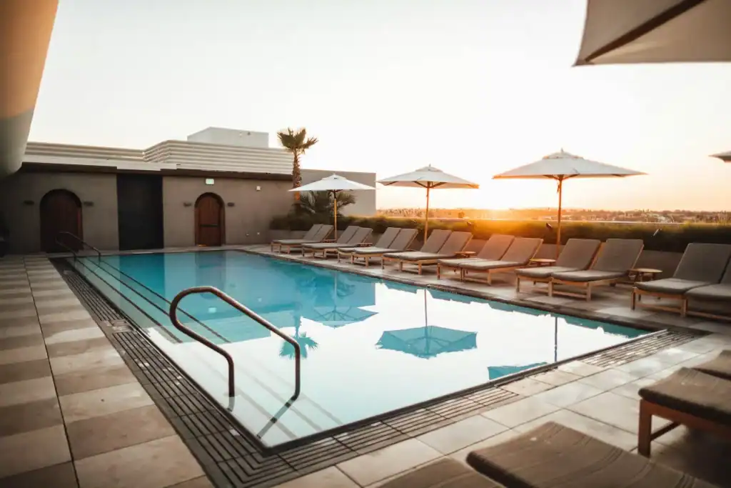Luxurious rooftop swimming pool with sun loungers and umbrellas during sunset, offering a perfect relaxing space in an upscale residential or hotel setting.