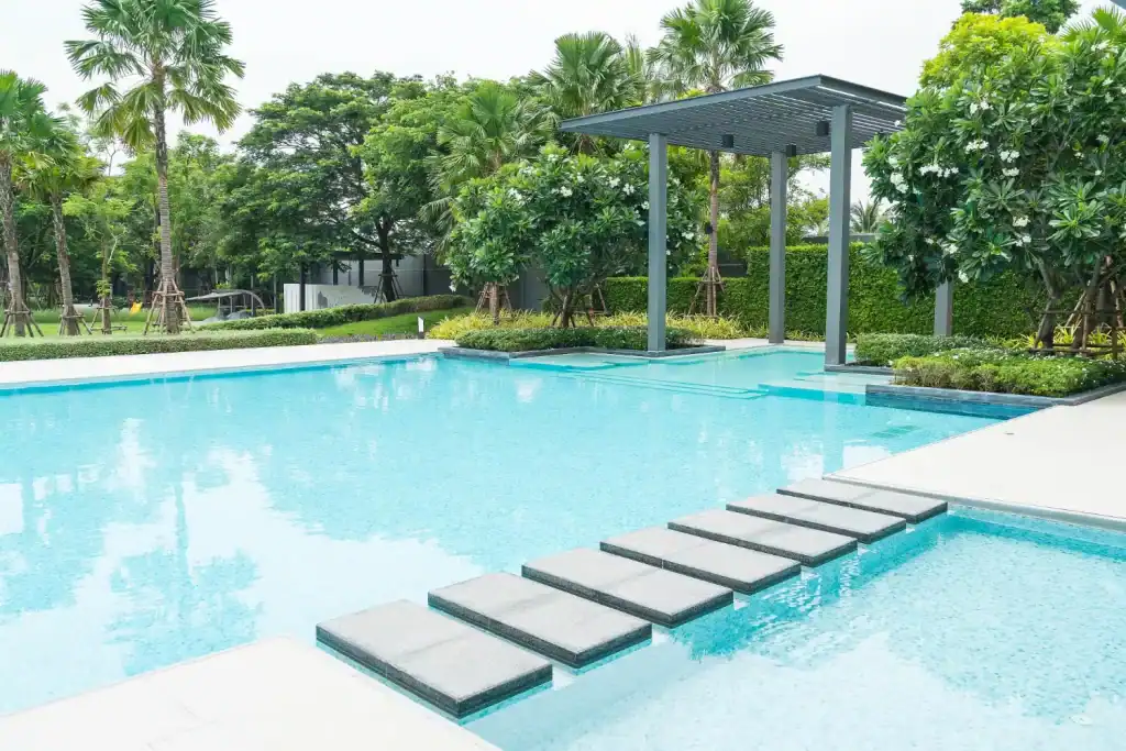 Lagoon-style swimming pool with modern design, floating steps, lush landscaping, and shaded seating area, perfect for backyard leisure and aesthetic appeal.