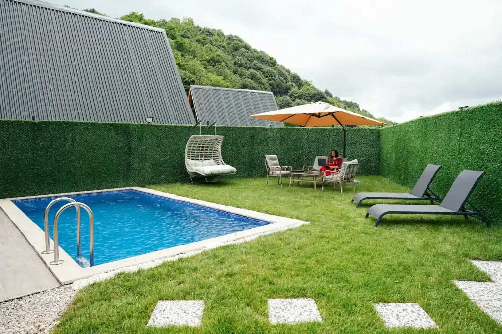 Luxurious backyard swimming pool with modern outdoor furniture, sun loungers, a shaded patio, and vibrant green fencing, creating an ideal space for relaxation and outdoor entertaining.