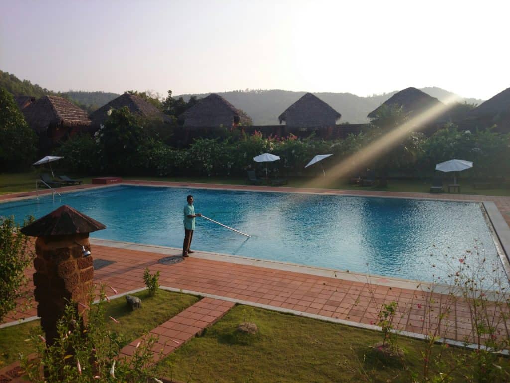 Bright and inviting backyard swimming pool with a professional cleaner. Surrounded by lush greenery, umbrellas, and scenic mountain views, showcasing expert pool building services.