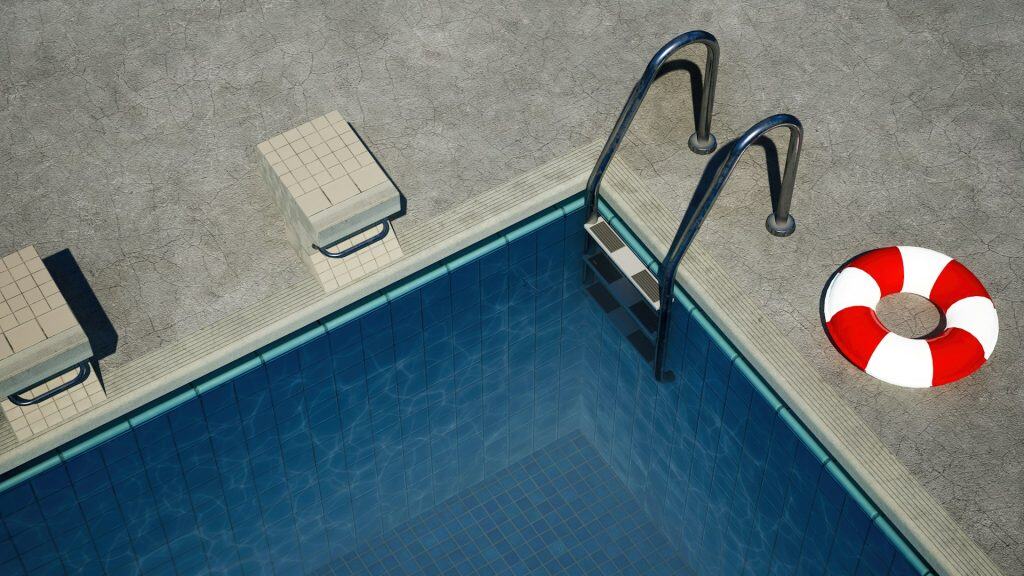 Aerial view of a swimming pool with safety ladder, life buoy, and tiled poolside area, showcasing professional pool construction and design services.