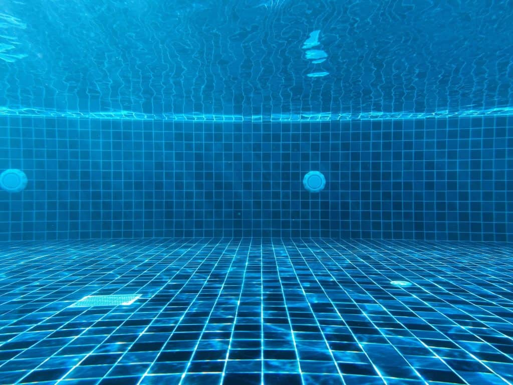 Vivid underwater view of a custom designed residential swimming pool with blue mosaic tiles, showcasing clear water and underwater lighting to create a luxurious swimming environment.