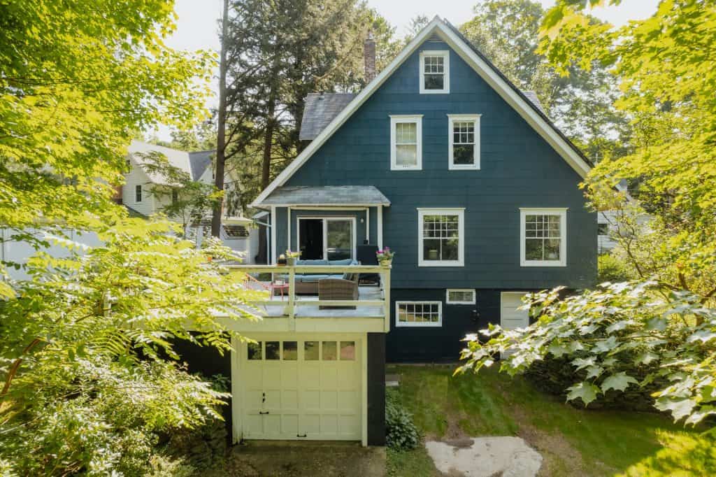 Blue house with a balcony and surrounding greenery in a residential neighborhood.