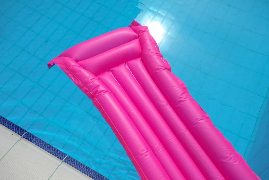 Bright pink inflatable pool float resting in a clear blue swimming pool, ideal for relaxing in the water during summer.