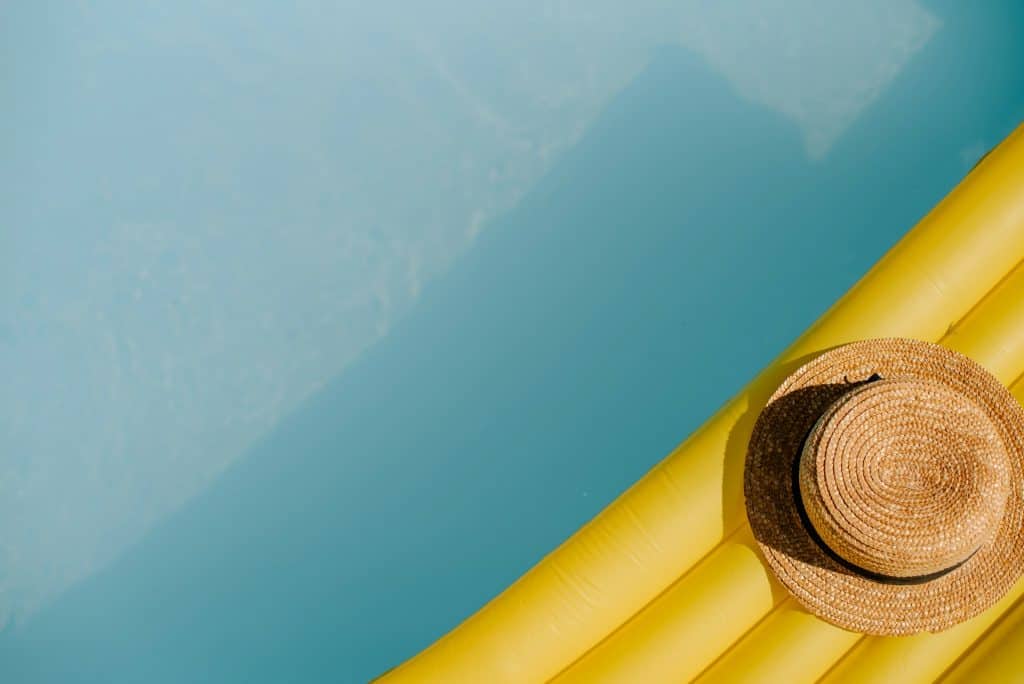 Bright yellow pool floaties and a straw sun hat placed on a poolside ladder, perfect for summer relaxation or pool parties. Create your ideal backyard oasis with professional pool construction services.