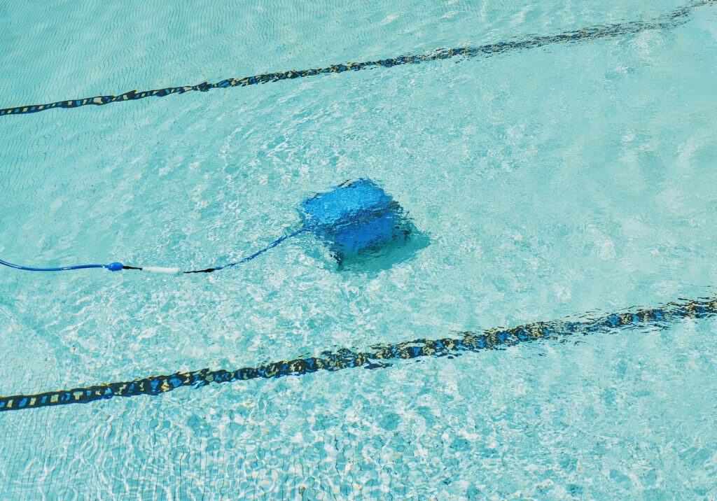 A robotic pool cleaner navigating the turquoise water of a backyard pool, ensuring optimal cleanliness and sparkling clarity for an enjoyable swimming experience.