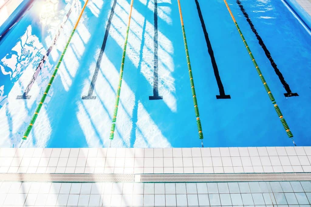 Bright blue swimming pool with lane markers, sunlight reflections, and a clean tiled edge, illustrating professional pool building services.