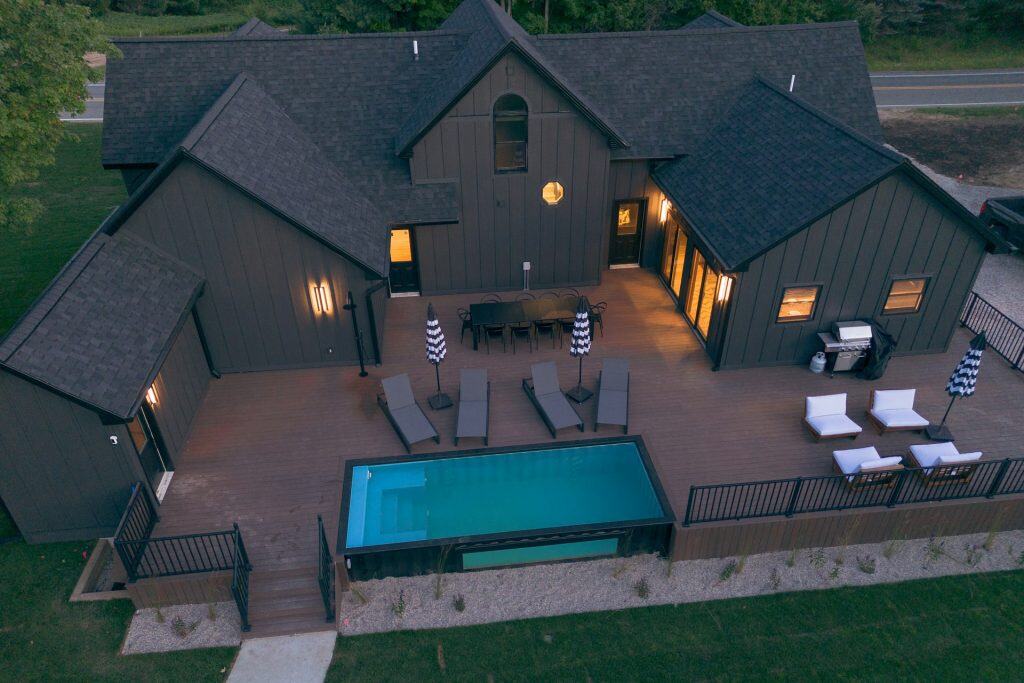 Aerial view of a modern house with a stunning outdoor pool, deck, and lounge area perfect for relaxing and entertaining. Custom pool builds by Duplessis Builders enhance your outdoor living space.